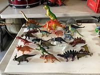 Top view all 25 plastic dinosaur figures on white surface