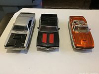 Front three-quarter view of all three diecast cars: silver Oldsmobile 442, black Camaro SS, orange Coronet Super Bee
