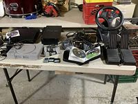 Overall lot view showing three consoles, steering wheel, pedals, game binder and cables