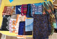Tabletop view of first group of folded scarves showing variety of colours, patterns and fabrics