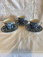 Three blue and white porcelain tea cups with saucers displayed on cloth