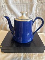 Full view left side of blue porcelain teapot on black base