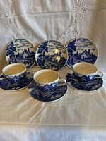Full view of three teacups with saucers and cake plates displaying blue transfer pattern