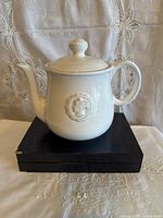 Side view of white Pottery Barn teapot showing medallion detail