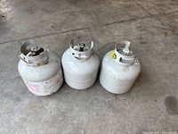 Three white 20-lb propane cylinders side by side on concrete floor
