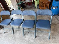 Four blue-upholstered metal folding chairs side by side