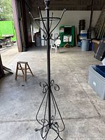 Full view of black metal coat rack showing hooks, scrollwork base, overall condition