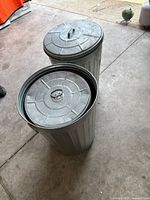 Two galvanized trash cans with lids on garage floor