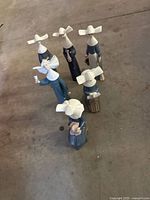 Top view of six ceramic nun figurines showing cornette headpieces and blue robes