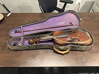 Open case showing violin with damaged strings and bow, purple lining