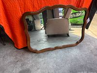 Front view of wood-framed mirror showing scalloped shape and reflection