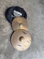Two Zildjian ZBT hi-hat cymbals and Sabian soft bag on concrete floor