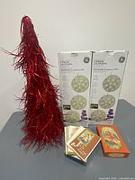 Group shot of all items: red tinsel tree, two GE LED sphere light boxes, stack and box of Christmas cards