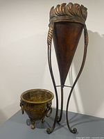 Tall metal cone planter on wrought stand next to smaller jardiniere