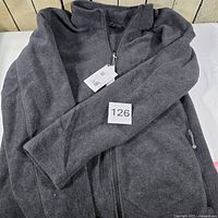 Full view of the dark grey fleece jacket laid flat showing zipper and pockets with tags attached