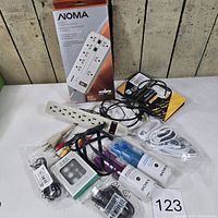 Overview of lot contents including boxed Noma surge protector, Sony earbuds, power bar, cables and accessories