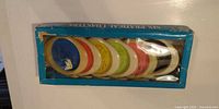 Boxed set showing stack of six coloured fish-shaped coasters through window