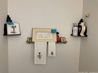 Wall view with central framed line art, two corner shelves, floating shelf, towels, vase, candle, small print, figurine