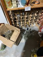 Wood wine rack filled with empty glass bottles, additional bottles in box and on floor