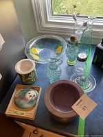 Group shot of all items on countertop: serving bowl, cruet, bottles, shaker, lavender bowl, covered jar, boxed paperweight
