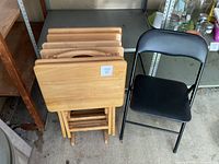 Wood TV trays stacked on stand beside black folding chair
