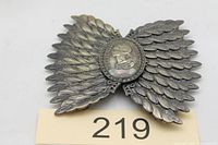 Front view of metal buckle displaying feathered wings and oval medallion