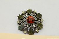 Front view showing orange centre stone, green stones, clear rhinestones and metalwork