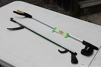 Two reacher grabber tools laid on table, showing full length and handle/jaw design