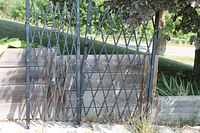 Full view of black metal accordion gate expanded beside planter