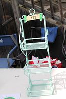 Front view of folding metal shelf showing three tiers and scrolled side arms