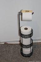 Full view of black metal freestanding toilet paper holder with rolls