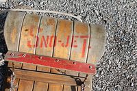 Curved front of wooden toboggan showing faded red Sno-Jet stencil and rope pull