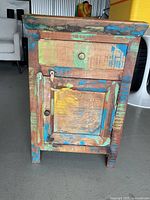 Front view of distressed wood wash stand showing drawer, cabinet door, hardware and multicolor paint