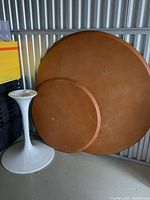 Large and small wooden circular tops leaning against wall beside pedestal base
