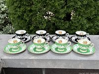 Front view of eight teacups with matching saucers (green and black designs) displayed outdoors