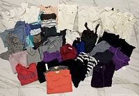 Full layout of entire clothing lot on floor showing variety of tops and pants