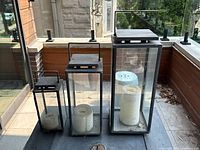 Three sizes of matching black metal and glass candle lanterns set outdoors