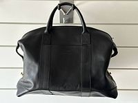 Full frontal view of black leather Aston Martin overnight bag
