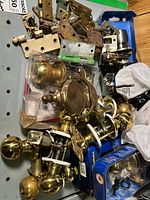 Pile of assorted door knobs, hinges, packaged lockset, door knocker
