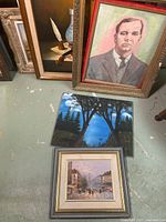 Group of four framed paintings and one canvas on floor: portrait, still life, forest landscape, street scene