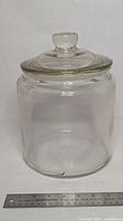 Full view of clear glass storage jar with lid and ruler for scale