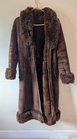 Front view of long dark brown shearling coat showing shawl collar, cuffs, hem trim