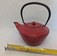 Full view of red cast iron teapot with tape for scale