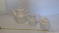 Front view of teapot, creamer and lidded sugar with measuring tape for scale