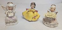 Front view of three 4-inch vintage ceramic angel figurines: June, yellow dress, November