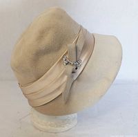 Left side view of cream felt cloche hat showing ribbon and rhinestone brooch