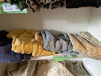 Shelf with multiple folded hand-knit sweaters in assorted colours