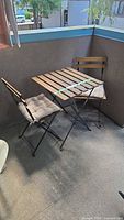 Wood slat folding table with two folding chairs and cushions on patio