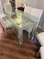 Full view of glass top dining table showing beveled edges, clear surface, and sculptural light wood bases