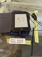 Kindle with flip cover on blue sleeve, charger, stylus visible